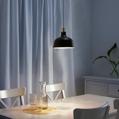 Black pendant light hangs above white dining table, contrasting industrial design with modern chairs and light curtains.