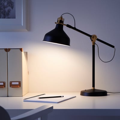 Black RANARP desk lamp with brass accent, providing focused light for workspace.