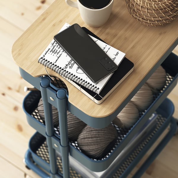 A multilevel cart with a wooden lid holds a tablet, remote, and notebook, showing its use for organising and storing items.