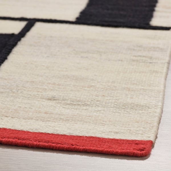 Flatwoven rug with beige wool surface, black rectangles, red edges, quality cotton, wool blend, stylish, durable.