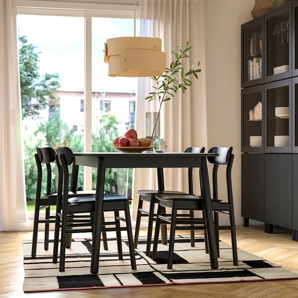 Dining room with black table, RASTPLATS rug, greenery, fruit, and building view.