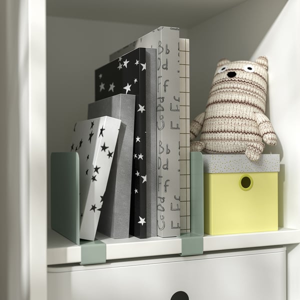 White shelf with star-patterned black boxes, knitted bear, and yellow boxed RELATERA book-ends.