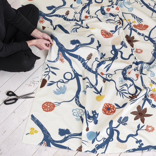 Person is crafting with colourful floral pattern fabric, scissors and pins nearby.
