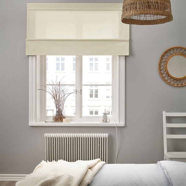 Bedroom with large grey window and beige roman blind. Basket pendant light above and white radiator below. Decorative vase on the window sill.