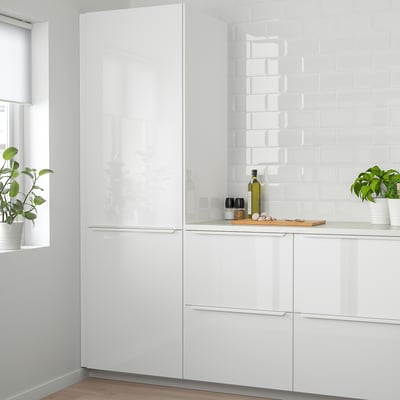 Modern white kitchen with glossy cabinets. Shiny drawers and tall units taller than window. Green plants on countertop.