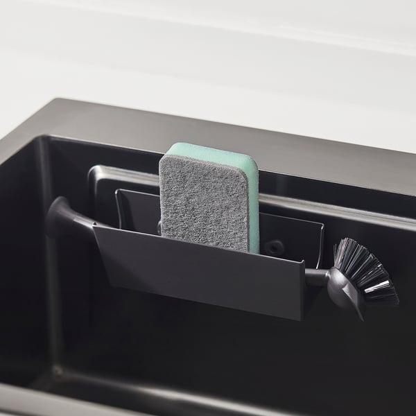 Black sink caddy with green sponge and scrub brush, showing organised storage near sink.