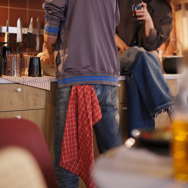Person wearing jeans and sweatshirt with a red checked tea towel hanging from their waist.