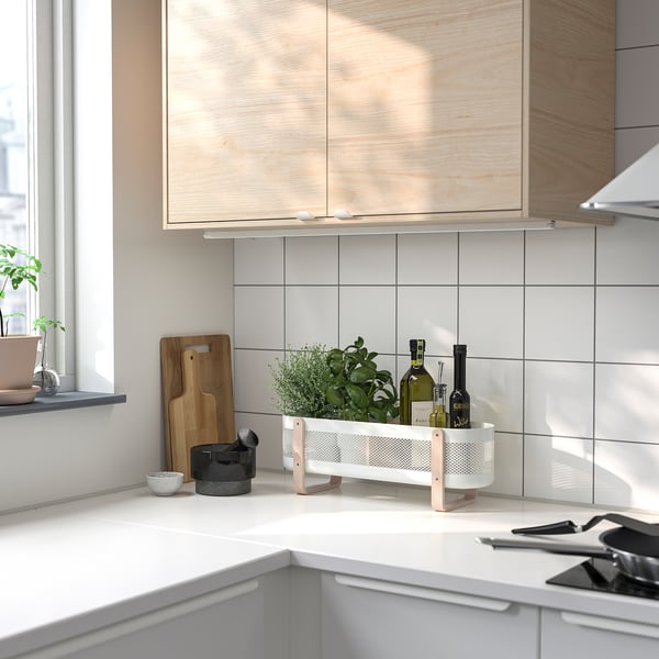A modern kitchen counter with RISATORP organizer, cutting boards, plant, and bottles. The white organizer with birch legs holds items neatly.