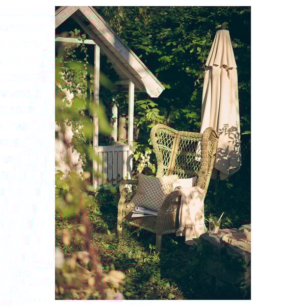 Green RISHOLMEN wicker chair in garden with open umbrella.