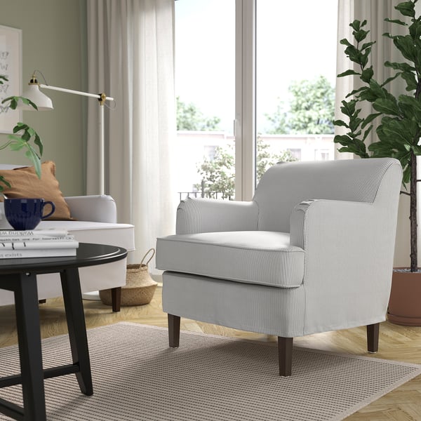 Modern living room with ROCKSJÖN grey striped armchair, wooden floor, plants, and white curtains.