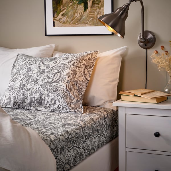 Cosy bed with RODGERSIA paisley sheet, cotton blend bedding, bedside lamp, and books.