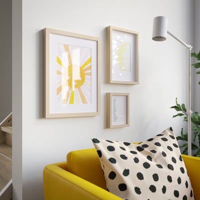 Yellow armchair with spotted pillow, three pictures on wall, lamp, plant.