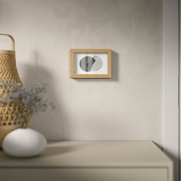 A minimalist room with abstract art on a grey wall, beige drawer, basket & flowers.
