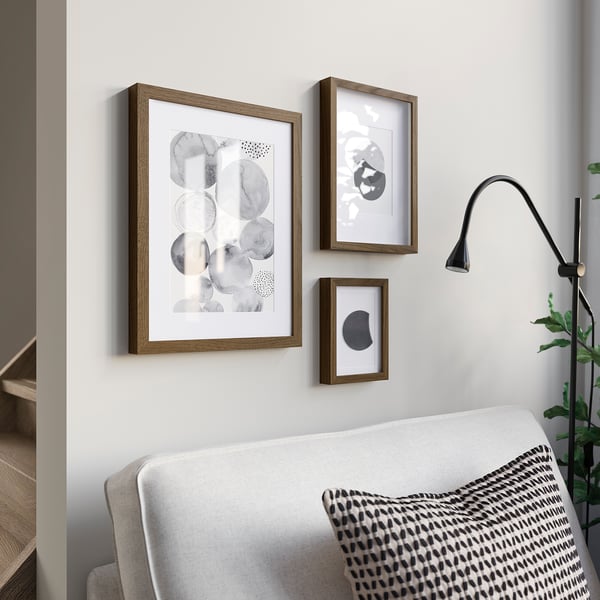 Three framed artworks in wooden bordersabove sofa; abstract, muted, bold circle. Black lamp to right, green plant beside.