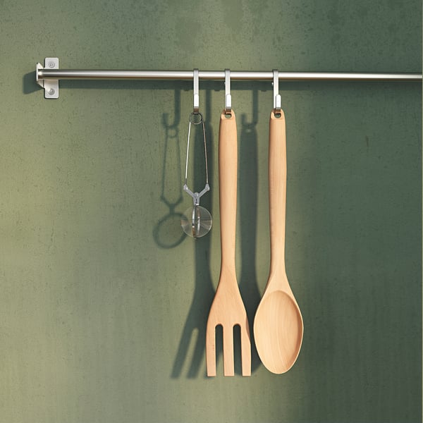 Two wooden kitchen utensils, a spoon and a fork, hang on hooks from a silver rod against a green wall.