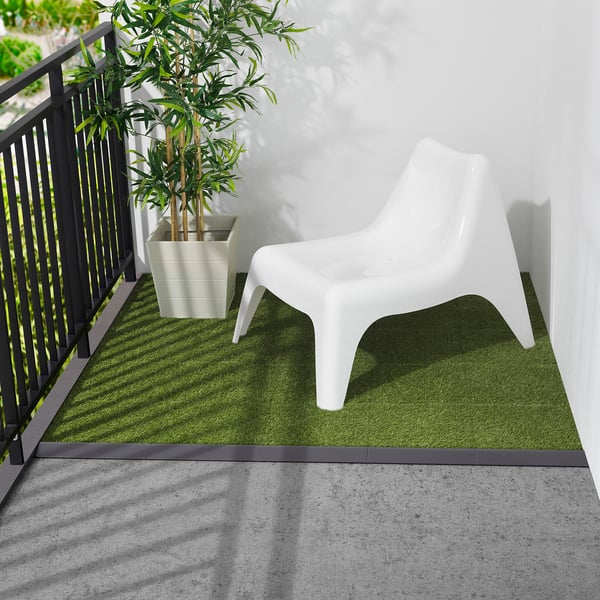 Small white plastic chair on green artificial grass mat near black railing.