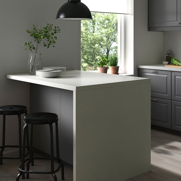 Modern kitchen island with white rounded edges, green base, two black stools, light fixture, grey cabinets, and wooden floor.