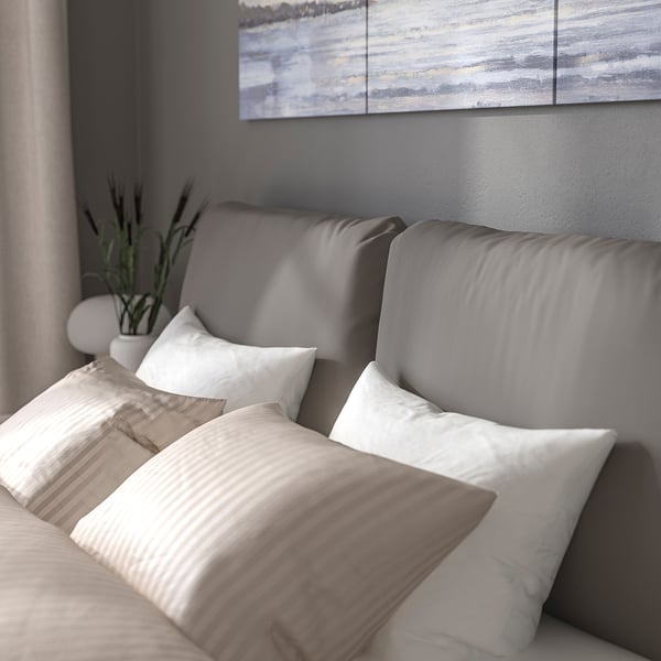 This image shows a modern upholstered bed frame with a sloped headboard and two large pillows for comfortable reading or relaxation.