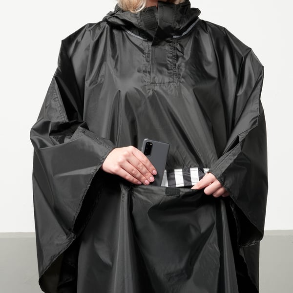 Person with SALTSTEN rain poncho holding phone in pocket.