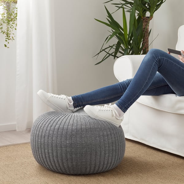 Person relaxes on white sectional, resting feet on grey knitted SANDARED pouffe, which serves as a footstool.