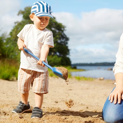 Child playing with blue sand toy on beach, pouring sand.