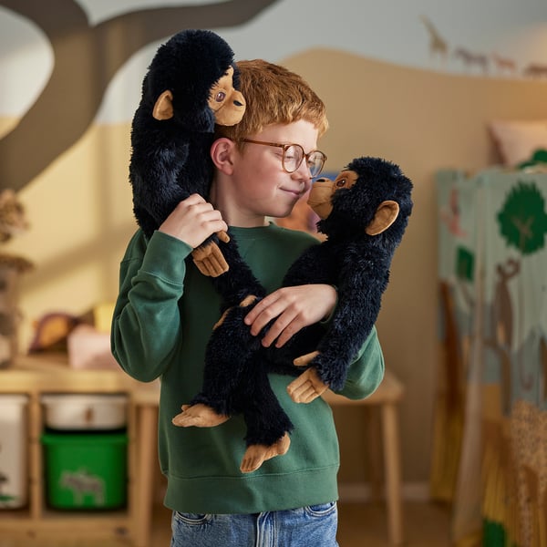 A boy hugs two soft toy chimpanzees in a cosy room. The chimps have touch-and-close fasteners on their hands and feet, enabling them to cling.