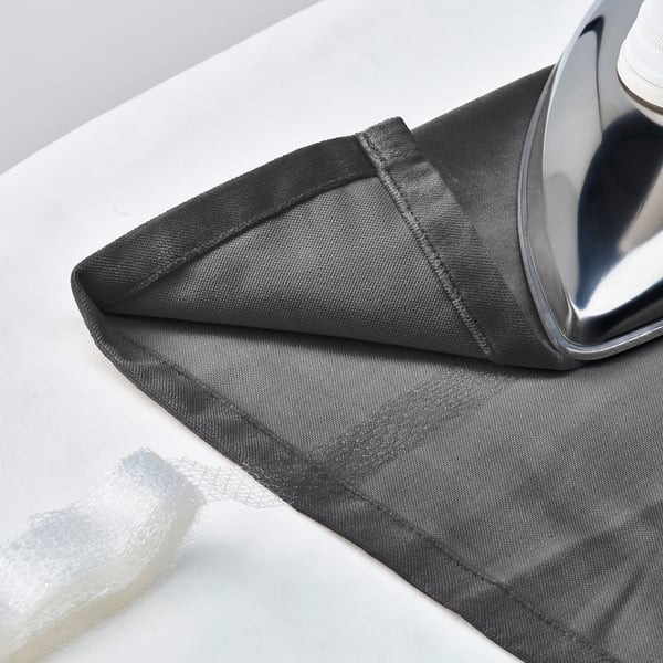 Curtain ironing: dark grey velvet curtain laid out, ready to be ironed to remove creases. Iron shown resting on folded edge.