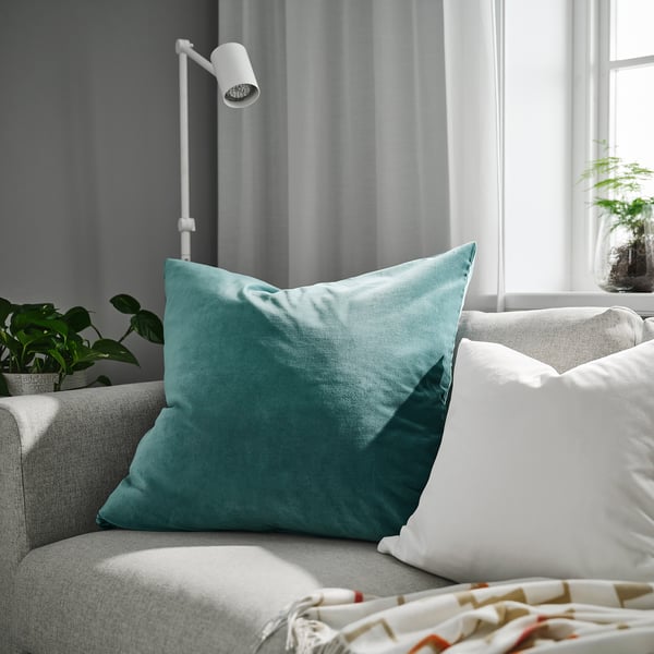 Teal SANELA cushion on grey couch. Soft velvet, ideal for reading in bed, surrounded by decor.
