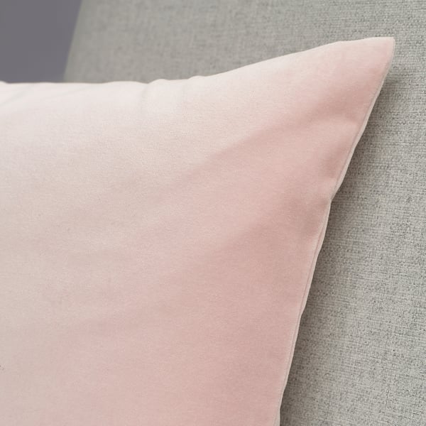 A plush, pastel pink cushion cover lying on a couch. The fabric appears soft and high-quality.