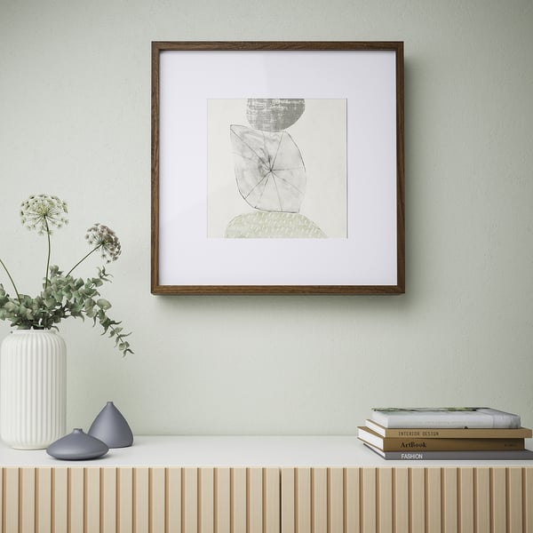 Abstract artwork in wooden frame on shelf, with vase and books.