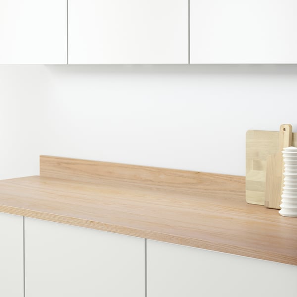 A light wood countertop with white cabinets; behind it, a light beige wall panel protects the wall from grease and splashes.