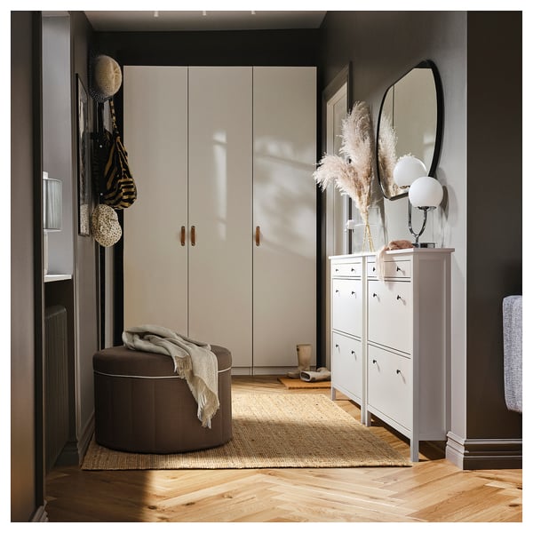 Modern entryway with white closet, round brown stool, white shoe cabinet, mirror, and dried floral decorations.
