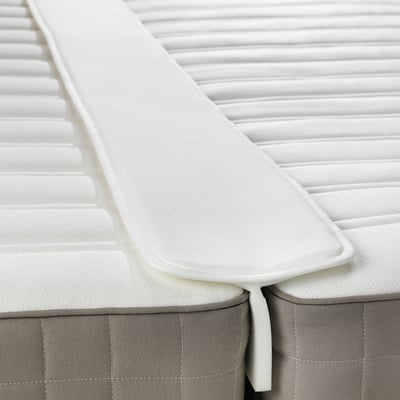Image depicts a white mattress gap filler, securing a crease between two mattresses.