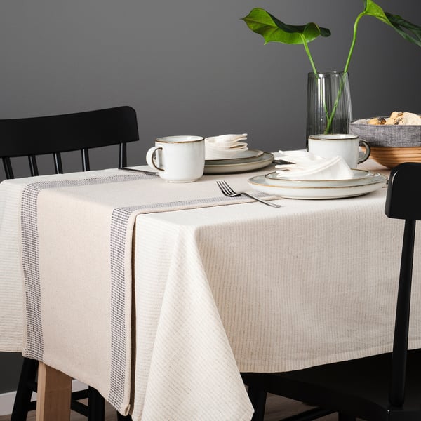 Table set with SILVERARV cloth, white cups, plates, and cutlery on dark chairs.