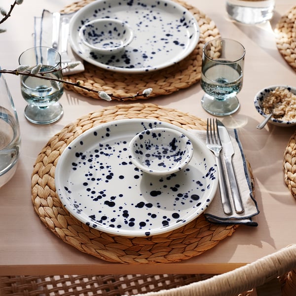 Table set with blue-speckled plates, cutlery, woven placemats, and glasses, ready for dining.