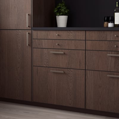 Dark wood SINARP kitchen cabinets, sleek & modern, with multiple drawers & shelves, surrounded by open spaces.