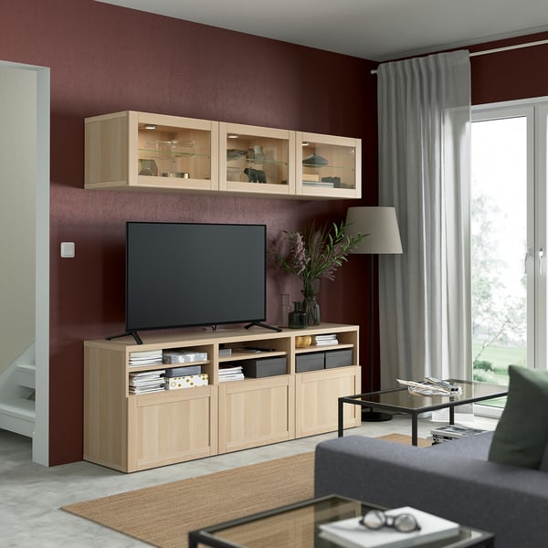 Large modern living room with red walls, featuring SINDVIK light oak tv stand & glass cabinet, grey sofa, coffee table, and large flat screen tv.