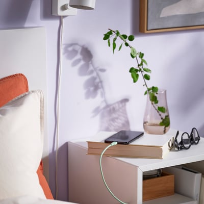 Bedroom bedside table with books, phone, vase, and glasses.