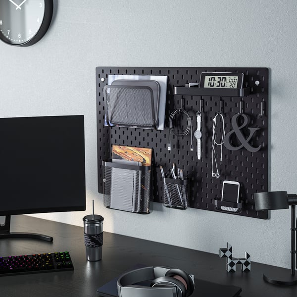 Black pegboard SKÅDIS organises office items, including files, pens, keys, and digital clock. Suitable for home office.