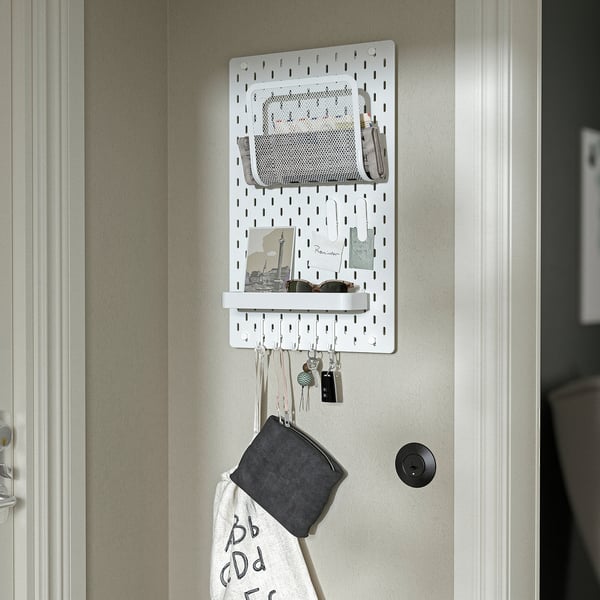 Wall-mounted pegboard organiser with hooks, pockets, and shelf, holding keys and bag.