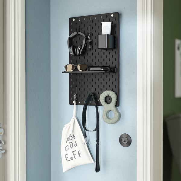 Black wall-mounted SKÅDIS organiser with hooks holding headphones, keys, glasses, and a bag.