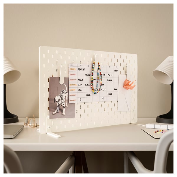 White SKÅDIS pegboard organiser with calendar, photos, and accessories on desk.