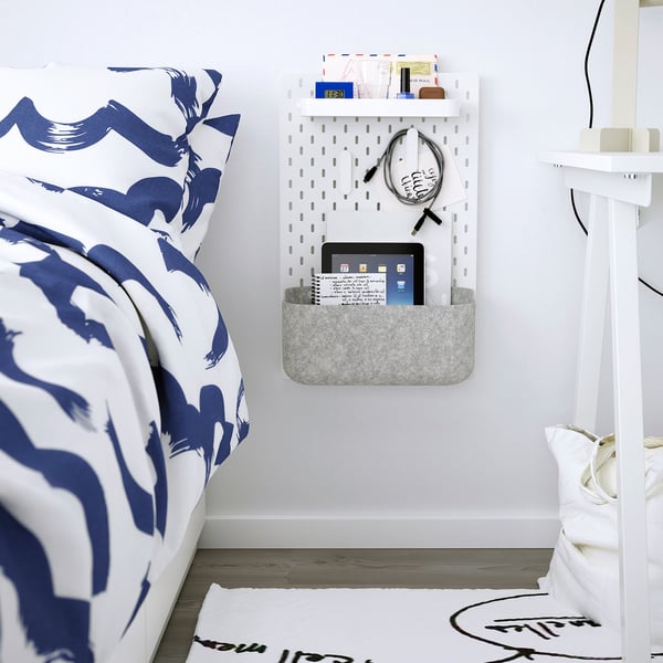 SKÅDIS basket on wall holds tablet, small items near patterned bed.