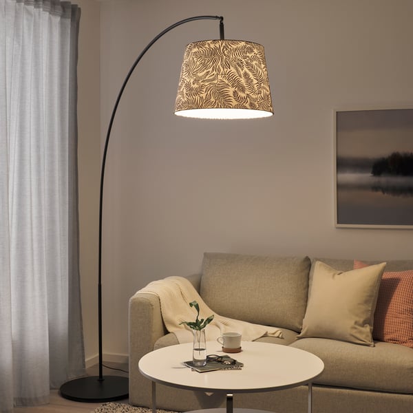 Black SKAFTET floor lamp with zebra-print shade hangs over beige sofa and white table. Soft, warm lighting illuminates cosy living room corner.