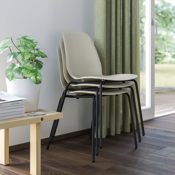 Stack of three white plastic chairs with black metal legs next to a table with a plant and books.