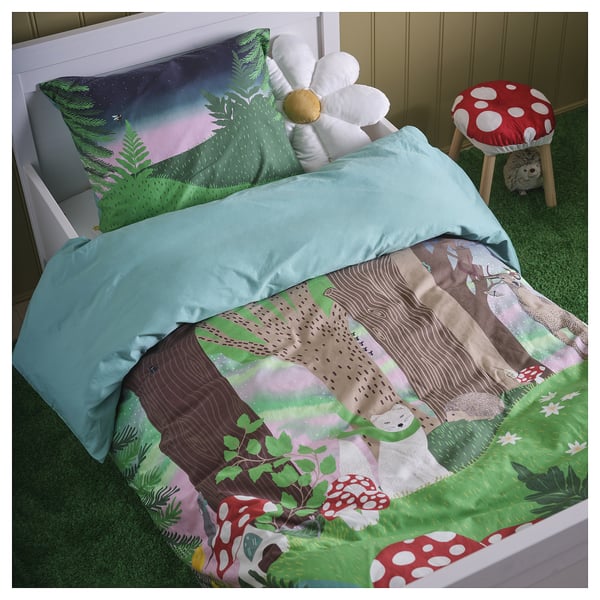 Bed with SKOGSDUVA green forest duvet, white pillows, red stool with hedgehog toy, and light blue bed duct showing forest scenes.
