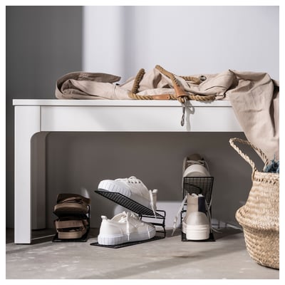 White SKOSTALL shoe rack stores multiple pairs. Top shelf holds dirt. Modern minimalist design. Woven basket on side.