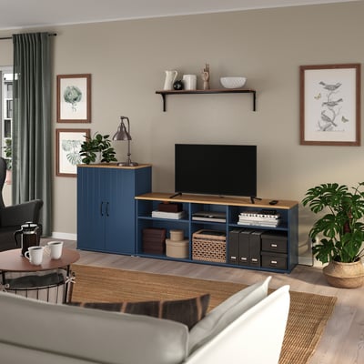 Cosy living room with grey curtains, a grey sofa, a blue tv stand with open and closed storage, a flat-screen tv, plants, and framed art.