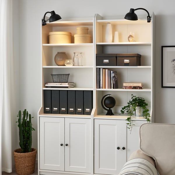 Wall-mounted black clamp lamp above white bookshelf, modern & focused lighting. Character count: 47