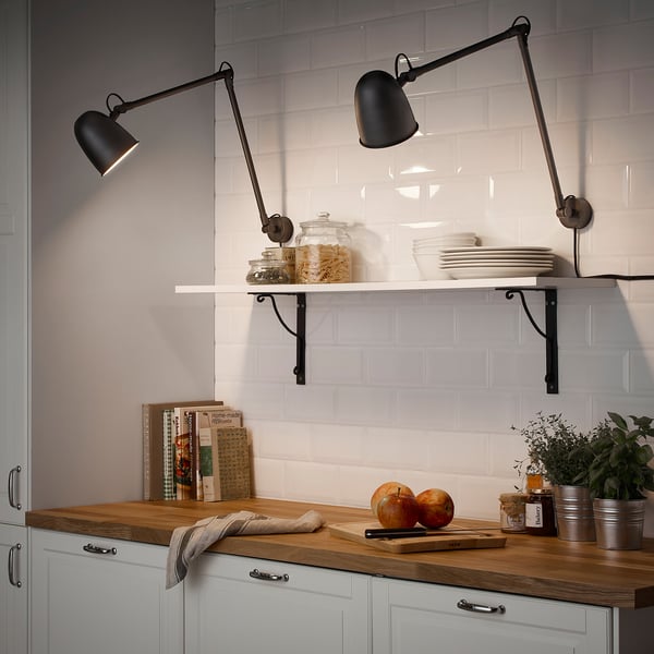 Two sleek wall lamps illuminate a kitchen counter with dishes, fruits, and herbs, creating a warm atmosphere.